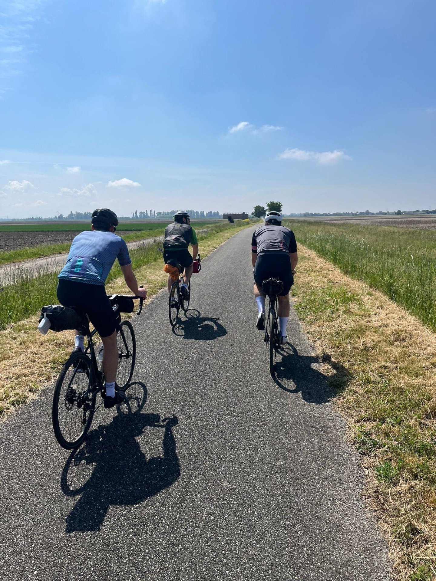 Three road cyclists on a European long-distance cycling route riding a quiet flat lane through open farmland